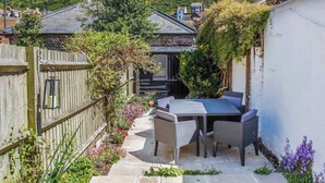 A patio area with a table and chairs, surrounded by a wooden fence and plants. - Charming Old Town Cottage With Modern Features (Hastings)