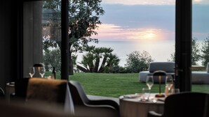 A dining area with a view of the sunset over the water, a grassy lawn, and outdoor seating.