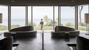 A modern interior with large windows, a central seating area, and a view of the sea.