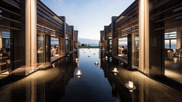 A modern hotel corridor with reflective flooring and glass doors leading to dining areas.