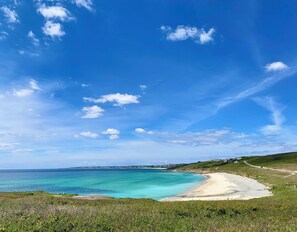 A coastal landscape with a clear sky, a sandy beach, and a grassy hill.