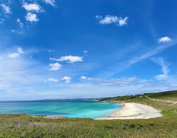 A coastal landscape with a clear sky, a sandy beach, and a grassy hill.