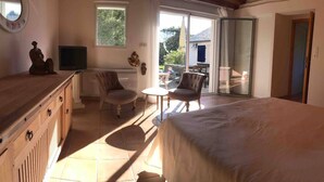 A bedroom with a bed, a TV, a chair, a small table, and a sliding glass door to a balcony. - Close to beaches (300 m) (plozevet)