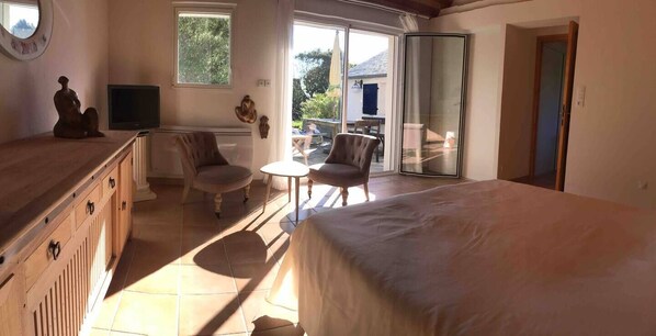 Une chambre avec un lit, une télévision, une chaise, une petite table et une porte-fenêtre coulissante donnant sur un balcon.