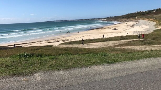 A beach with a road in the foreground, a sandy shore, and a few people walking. - Close to beaches (300 m) (plozevet)