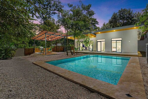 Une maison moderne dotée d’une piscine, d’un patio couvert et d’une grande fenêtre donnant sur la piscine.