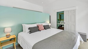 A modern bedroom with a large bed, a bedside table with a lamp, and a door leading to a bathroom. - Home with the best pool 5 min drive to town (tamarindo)