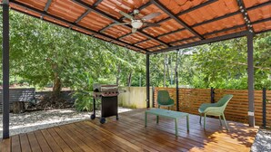 An outdoor patio with a wooden deck, a barbecue grill, a table, and two chairs. - Home with the best pool 5 min drive to town (tamarindo)
