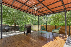 Une terrasse extérieure avec une plateforme en bois, un barbecue, une table et deux chaises.