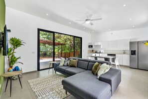 A modern living room with a grey sectional sofa, a small round table, and a large window overlooking a garden.
