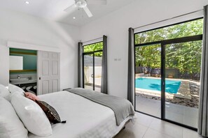 Une chambre dotée d’un grand lit, offrant une vue sur une piscine et donnant sur l’extérieur grâce à une porte-fenêtre coulissante.