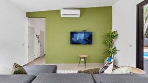 A modern living room with a green accent wall, a mounted TV, a potted plant, and a grey sofa. - Home with the best pool 5 min drive to town (tamarindo)