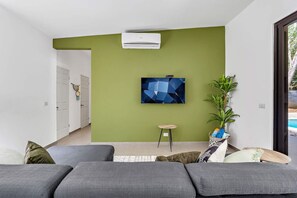 A modern living room with a green accent wall, a mounted TV, a potted plant, and a grey sofa. - Home with the best pool 5 min drive to town (tamarindo)