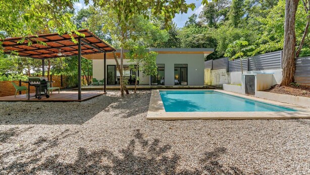 A modern outdoor pool area with a covered patio, a barbecue setup, and a house in the background. - Home with the best pool 5 min drive to town (tamarindo)
