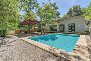 Une piscine agrémentée d’une pergola, d’un patio couvert et d’une maison moderne dotée de grandes fenêtres.