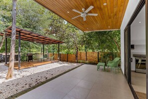 Un patio extérieur couvert, doté d’un ventilateur de plafond, d’un barbecue et d’un espace détente avec des chaises.