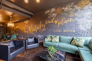 Un espace de détente moderne avec un mur en briques, un canapé vert, des fauteuils en cuir noir et une table basse en marbre.