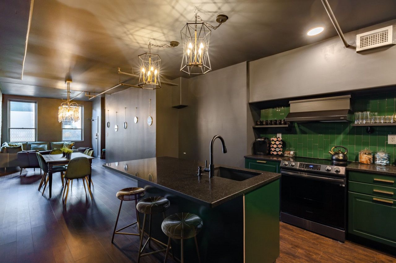 Une cuisine moderne dotée d’un grand îlot central, de meubles de couleur verte et de luminaires suspendus.