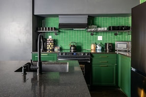 Une cuisine avec des meubles de rangement verts, une cuisinière noire, une bouilloire et un four à micro-ondes.