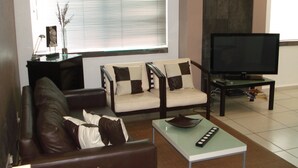 A living room with a sofa, armchair, and a coffee table. There is a television and a small table with decorative items. - Central located luxury studio, steps to all bars & restaurants,  (Puerto Vallarta)