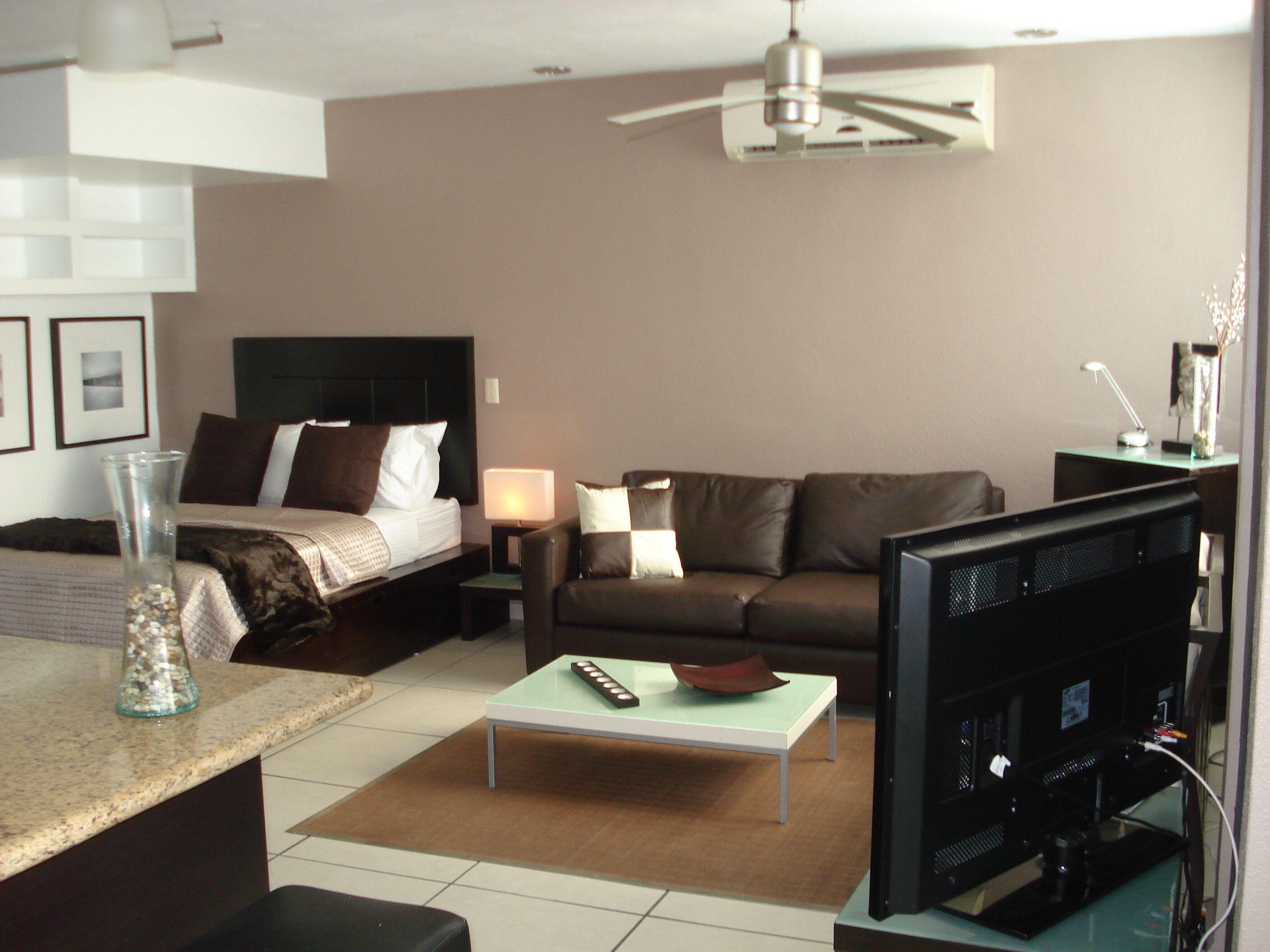 Camera d'albergo con un letto, un divano, un tavolino, una TV e una ventola a soffitto.