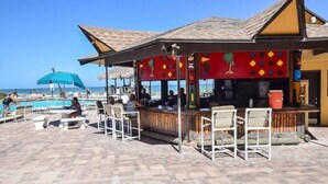 Un bar situé en bord de mer, avec des tables à l’extérieur et une piscine en arrière-plan.