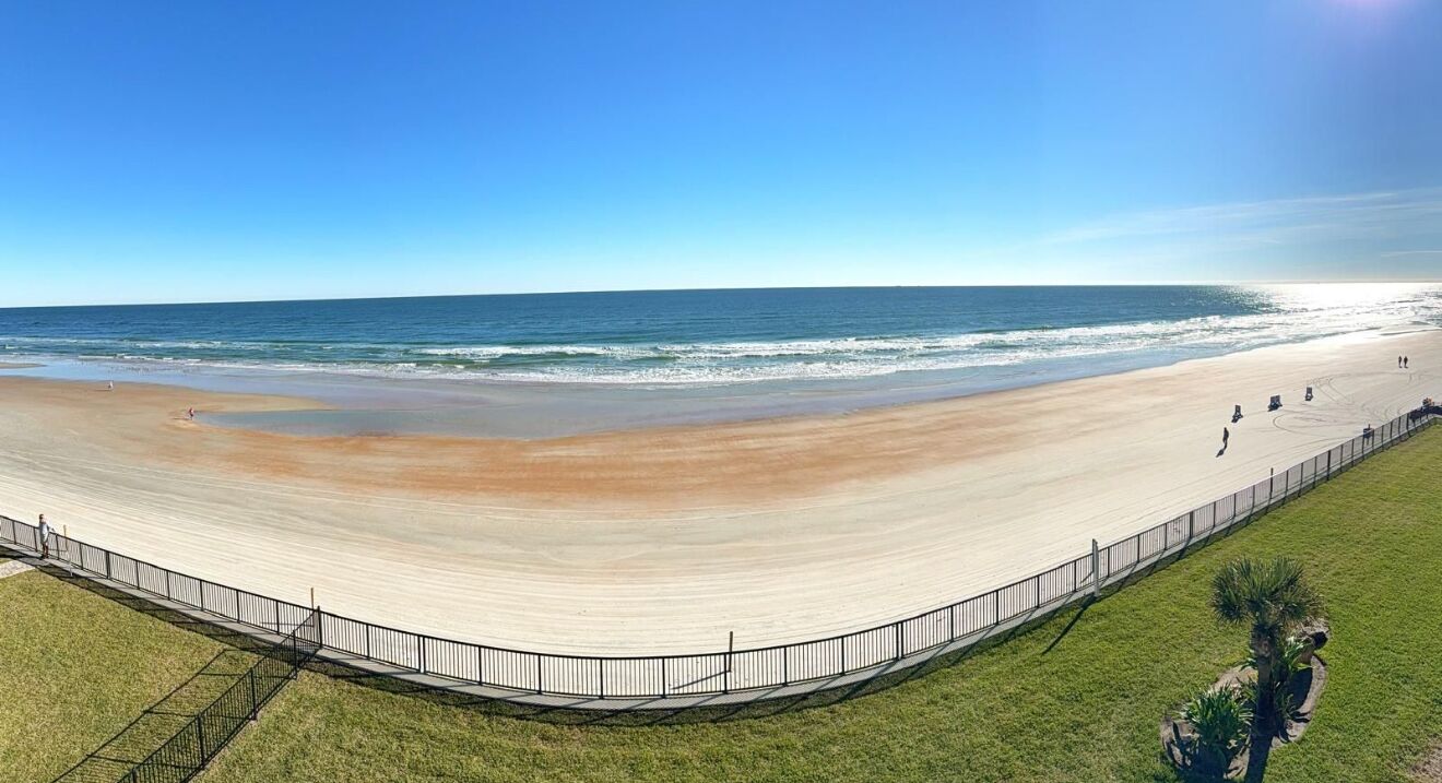 A beach with a curved walkway, a grassy area, and a fence.