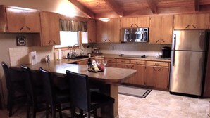 Una cocina con gabinetes de madera, un refrigerador de acero inoxidable, un lavamanos y una zona de comedor con sillas.