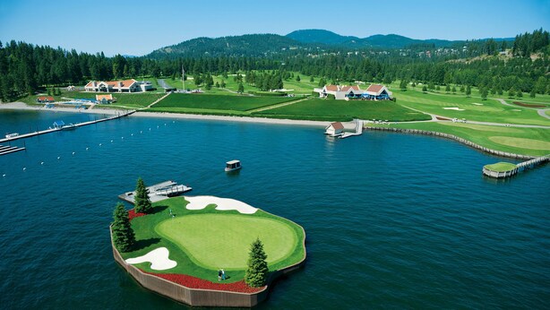 Vista aérea de un campo de golf con un cuerpo de agua, un club de campo y zonas verdes circundantes.