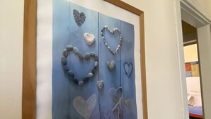 A framed artwork with heart shapes made from stones and twine on a blue background. - Sea Villa (Baia Verde)