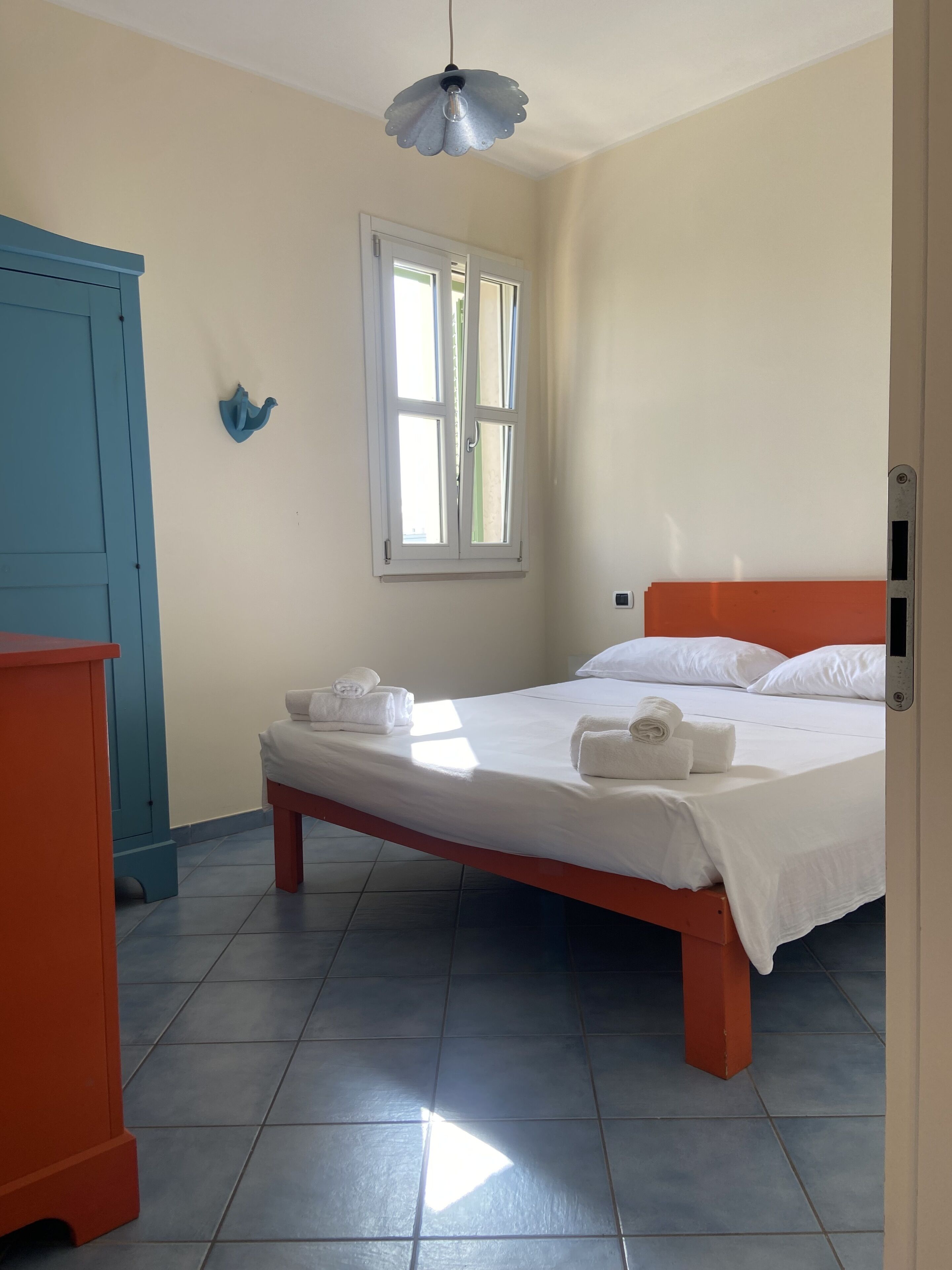 A bedroom with a bed, a window, a blue cabinet, and a red dresser.