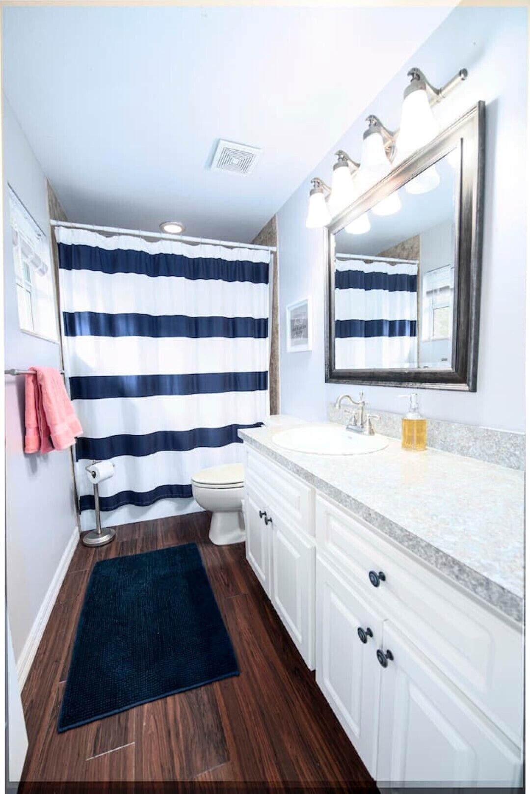 A bathroom with a striped shower curtain, a white sink, a mirror, and wooden flooring.
