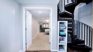 A hallway with a carpeted floor, a white door, and a staircase with a black railing.