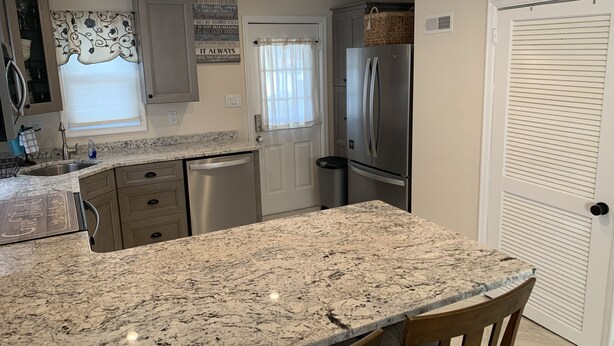 A kitchen with granite countertops, stainless steel appliances, and a window with a decorative curtain.