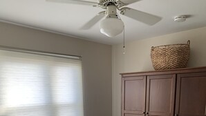 A bedroom with a bed, a ceiling fan, a window with blinds, a wooden wardrobe, and a woven basket on top.