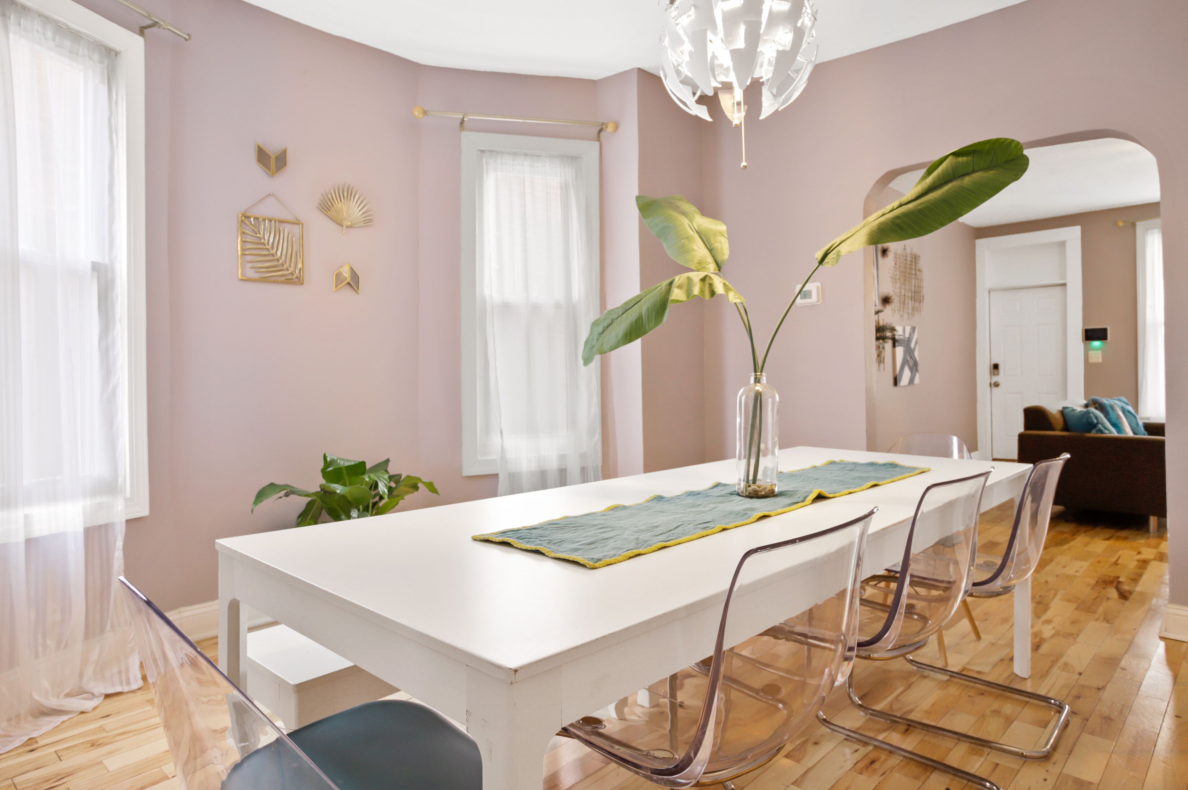 A dining area with a white table, clear chairs, and a vase with a plant.