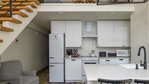 A modern kitchen with white cabinets, a refrigerator, stove, microwave, and a dining area with a white island and bar stools. - Main Street Farmhouse. City Retreat by Hollyhock (Louisville)