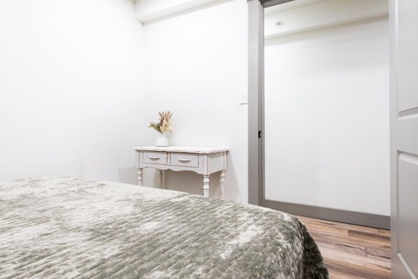 A bedroom with a bed, a small white dresser with drawers, a vase with flowers, and a wooden floor.