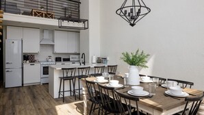 A modern kitchen with white cabinets, a dining area with a wooden table and black chairs, and a hanging light fixture. - Main Street Farmhouse. City Retreat by Hollyhock (Louisville)