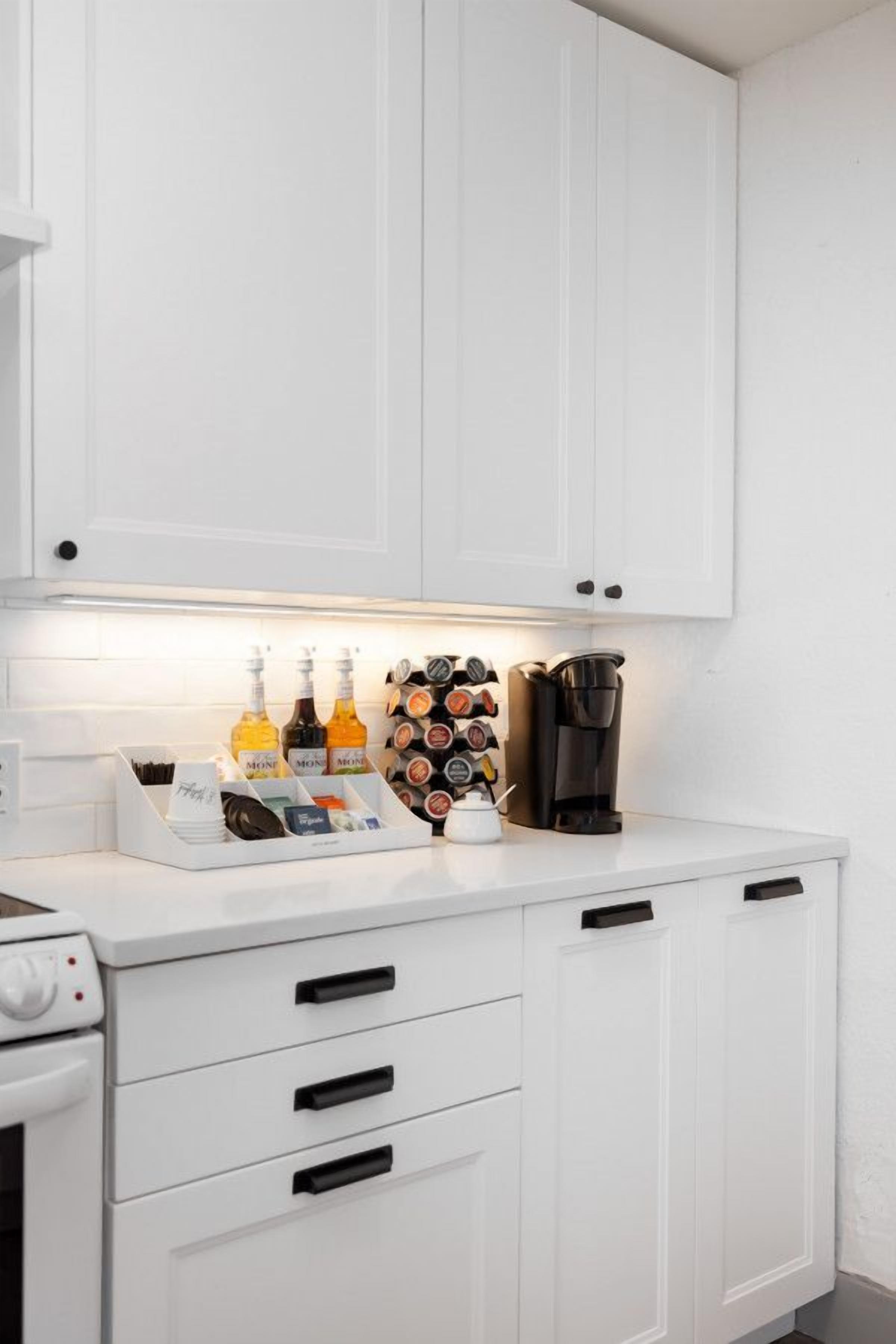 A kitchen with white cabinets, a coffee maker, and a bottle holder with various bottles.