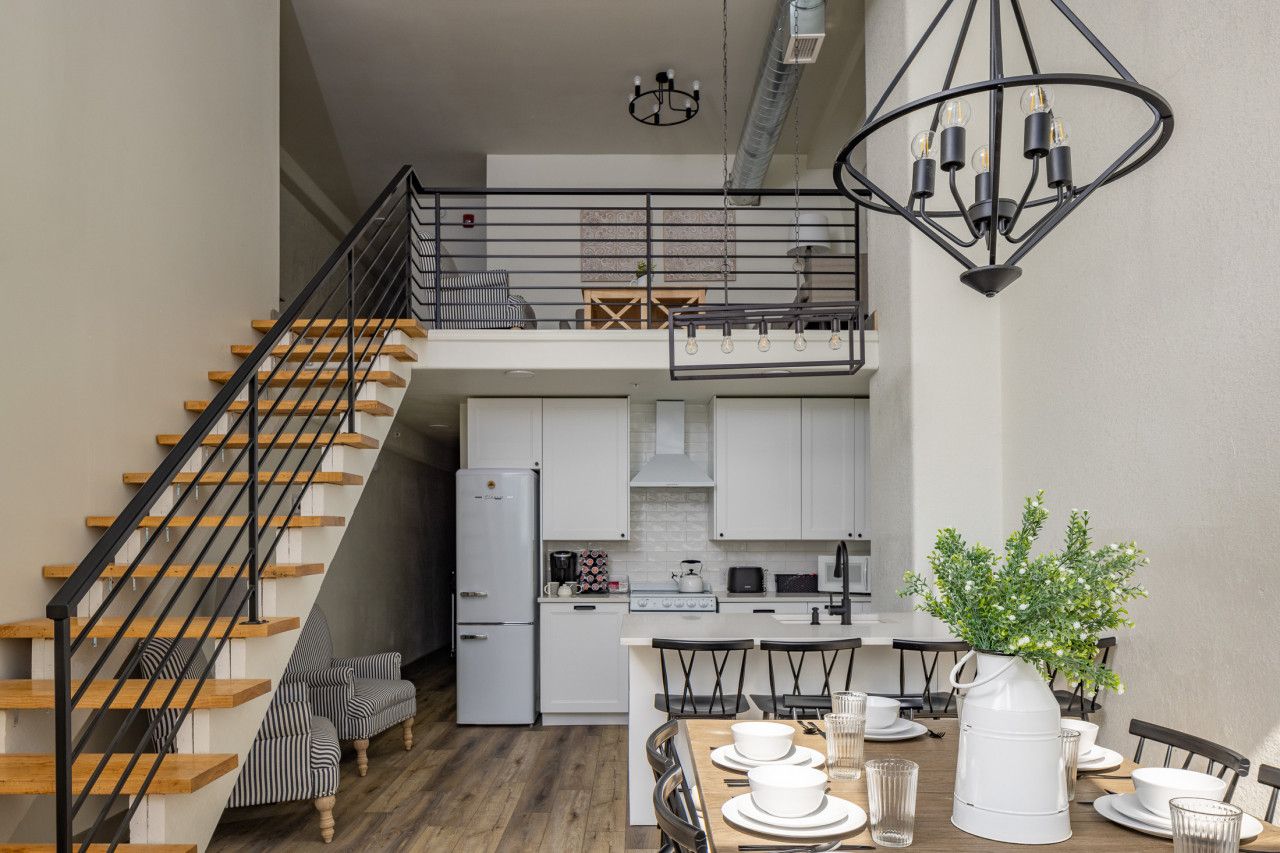 A modern kitchen with a central island, a dining area with a table set for two, and a staircase leading to an upper level.