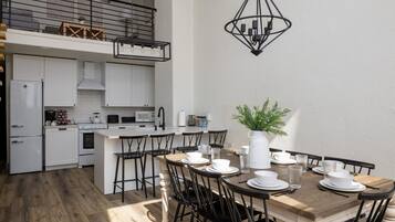 A modern kitchen with white cabinets, a dining area with a wooden table and black chairs, and a hanging light fixture.