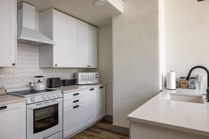 A modern kitchen with white cabinetry, a stove, microwave, and a kettle.
