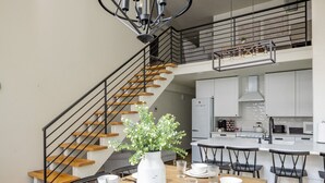 A modern kitchen with white cabinets, a central island, and a dining area with a wooden table and black chairs. - Main Street Farmhouse. City Retreat by Hollyhock (Louisville)