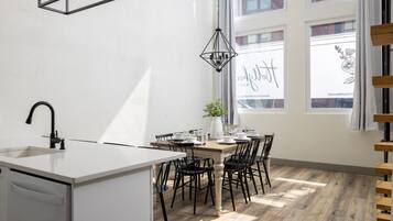A modern kitchen with a white countertop, black chairs, a wooden dining table, and a hanging light fixture.