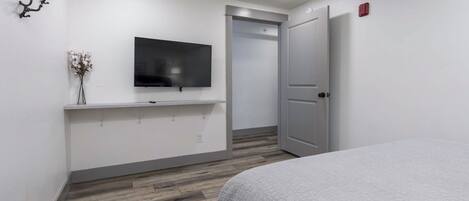 Een slaapkamer met een bed, een wandtelevisie, een deur en een wandplank met een vaas.