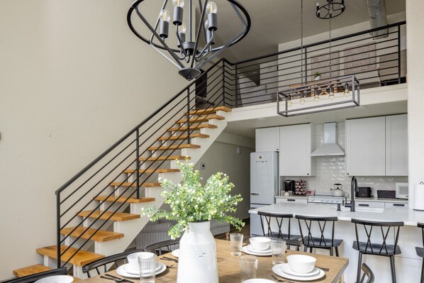A modern kitchen with white cabinets, a central island, and a dining area with a wooden table and black chairs.