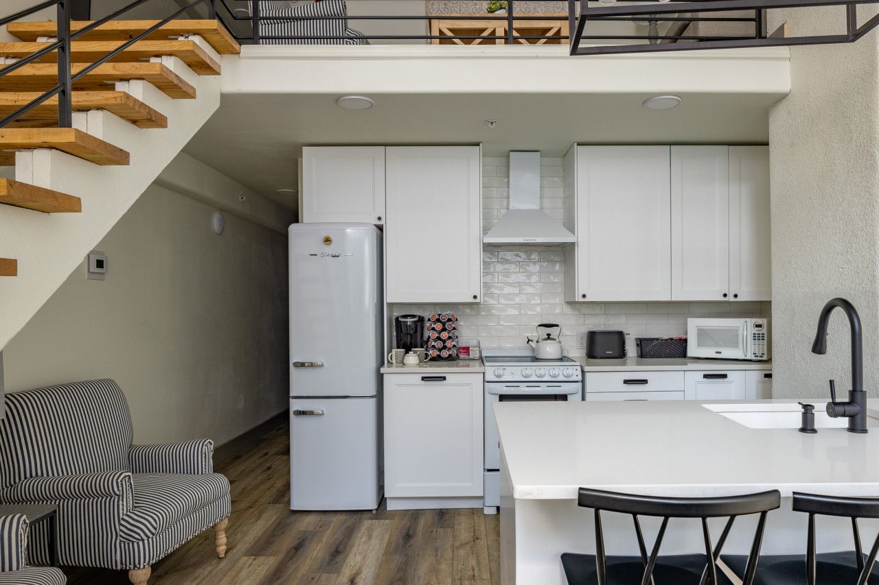 Une cuisine moderne avec des meubles blancs, un réfrigérateur, une cuisinière, un four à micro-ondes et un coin repas comprenant un îlot central blanc et des tabourets de bar.