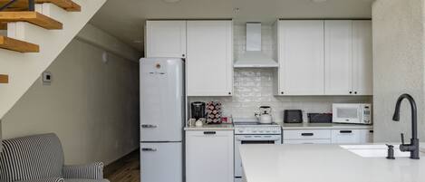Une cuisine moderne avec des meubles blancs, un réfrigérateur, une cuisinière, un four à micro-ondes et un coin repas comprenant un îlot central blanc et des tabourets de bar.