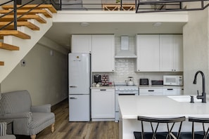 A modern kitchen with white cabinets, a refrigerator, stove, microwave, and a dining area with a white island and bar stools.